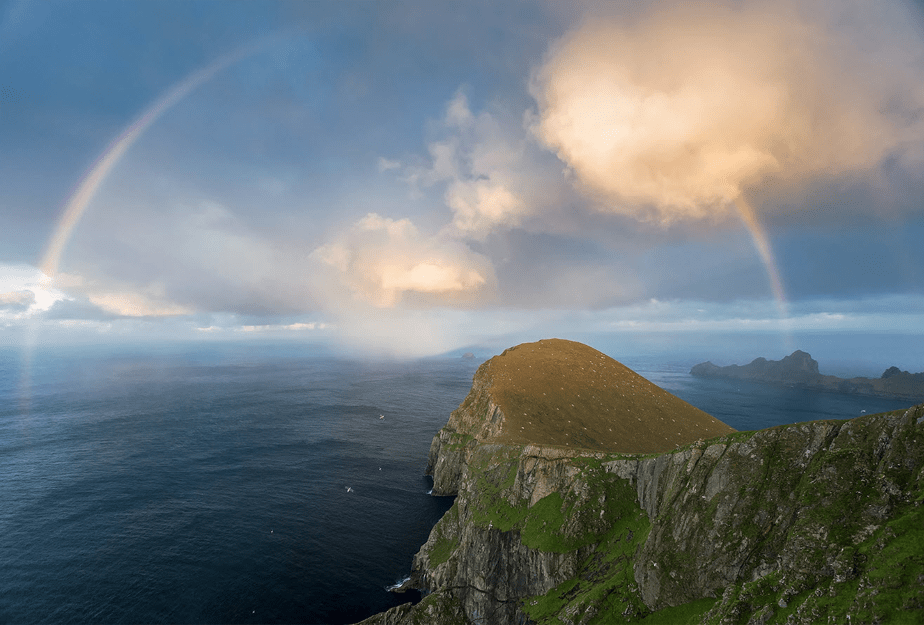 een volle regenboog verschijnt boven de zee aan het einde van een bergklif
