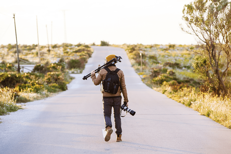 fotograaf lopen op een onverharde weg met een statief en camera